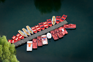 Ein Bootssteeg im Wasser, umringt von roten Booten. Blick von oben